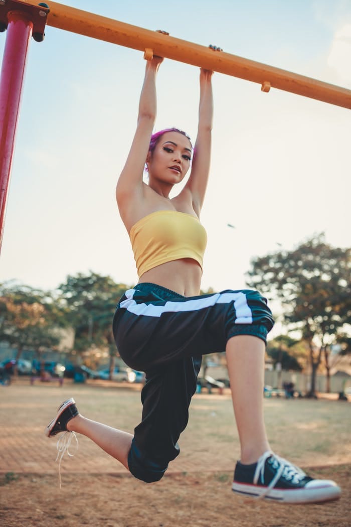A fit woman in casual activewear hanging from a playground bar, showcasing strength and style.